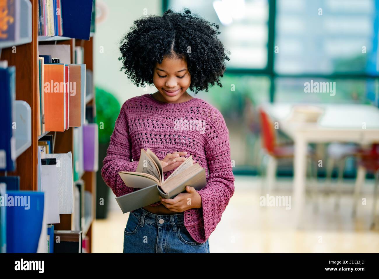 Black Child parcourant les pages de livre à l'intérieur de la bibliothèque de l'école. Moment de curiosité apprentissage indépendant confiance concept d'éducation à la diversité. Auto-apprentissage Banque D'Images