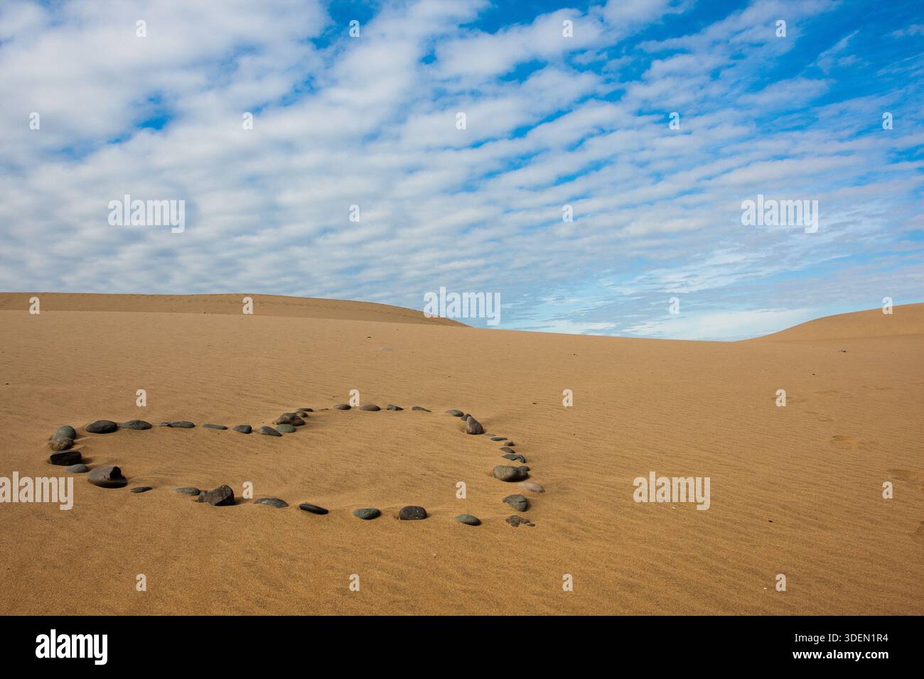 Forme de coeur en pierres sur sable avec ciel bleu et nuages blancs sur fond, espace de copie Banque D'Images