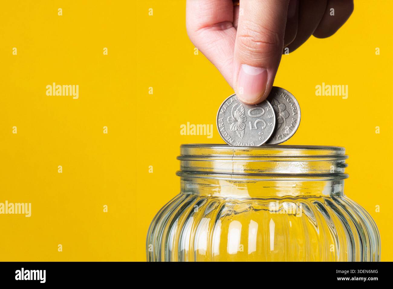 Main économiser de l'argent en déposant des pièces dans un bocal en verre transparent Banque D'Images