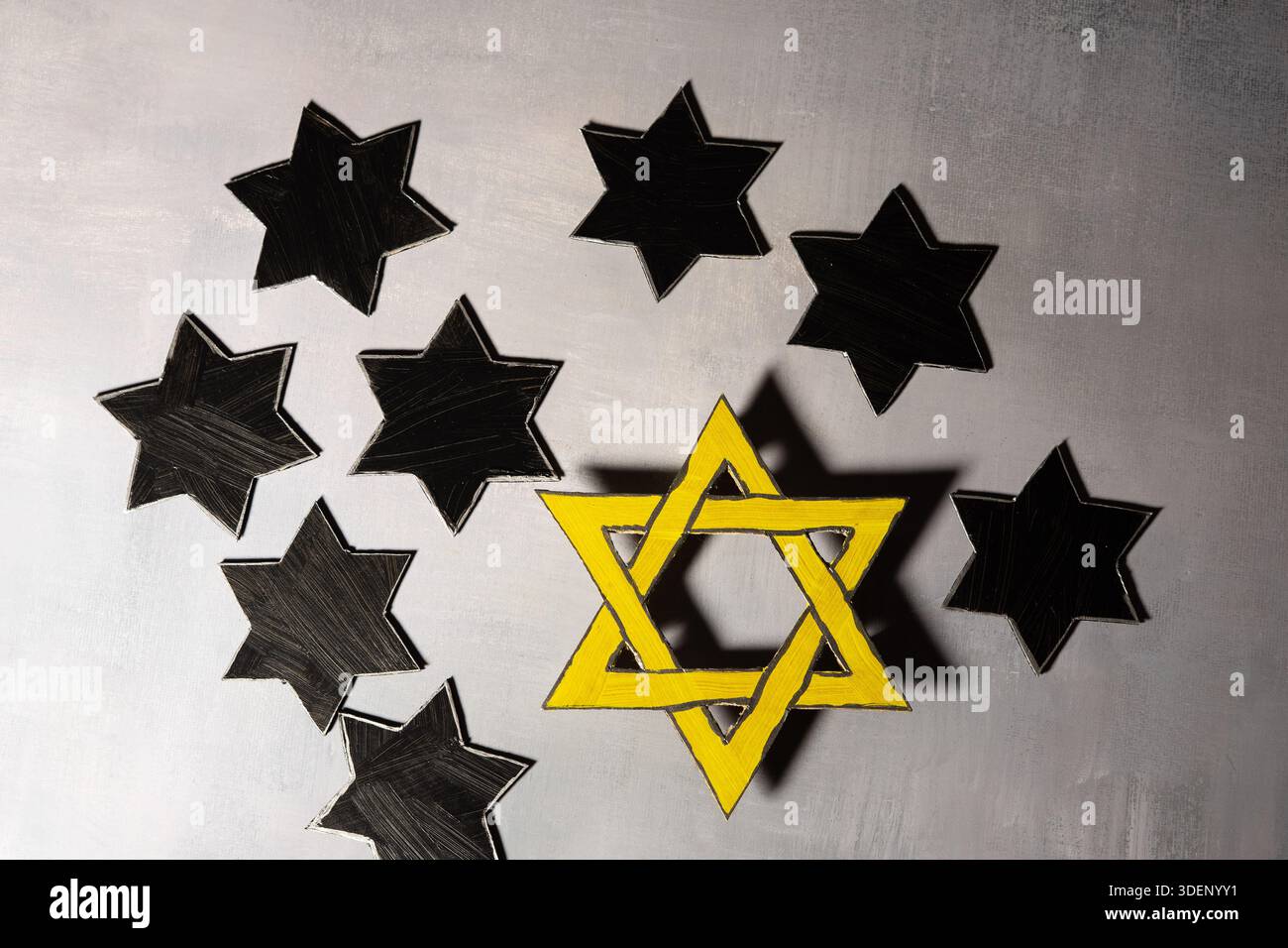 Une étoile jaune de David se trouve parmi plusieurs étoiles noires sur une surface grise, symbolisant le souvenir de l'Holocauste et l'identité juive. Banque D'Images