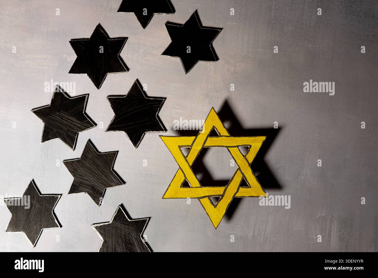 Une étoile jaune de David se trouve parmi plusieurs étoiles noires sur une surface grise, symbolisant le souvenir de l'Holocauste et l'identité juive. Banque D'Images