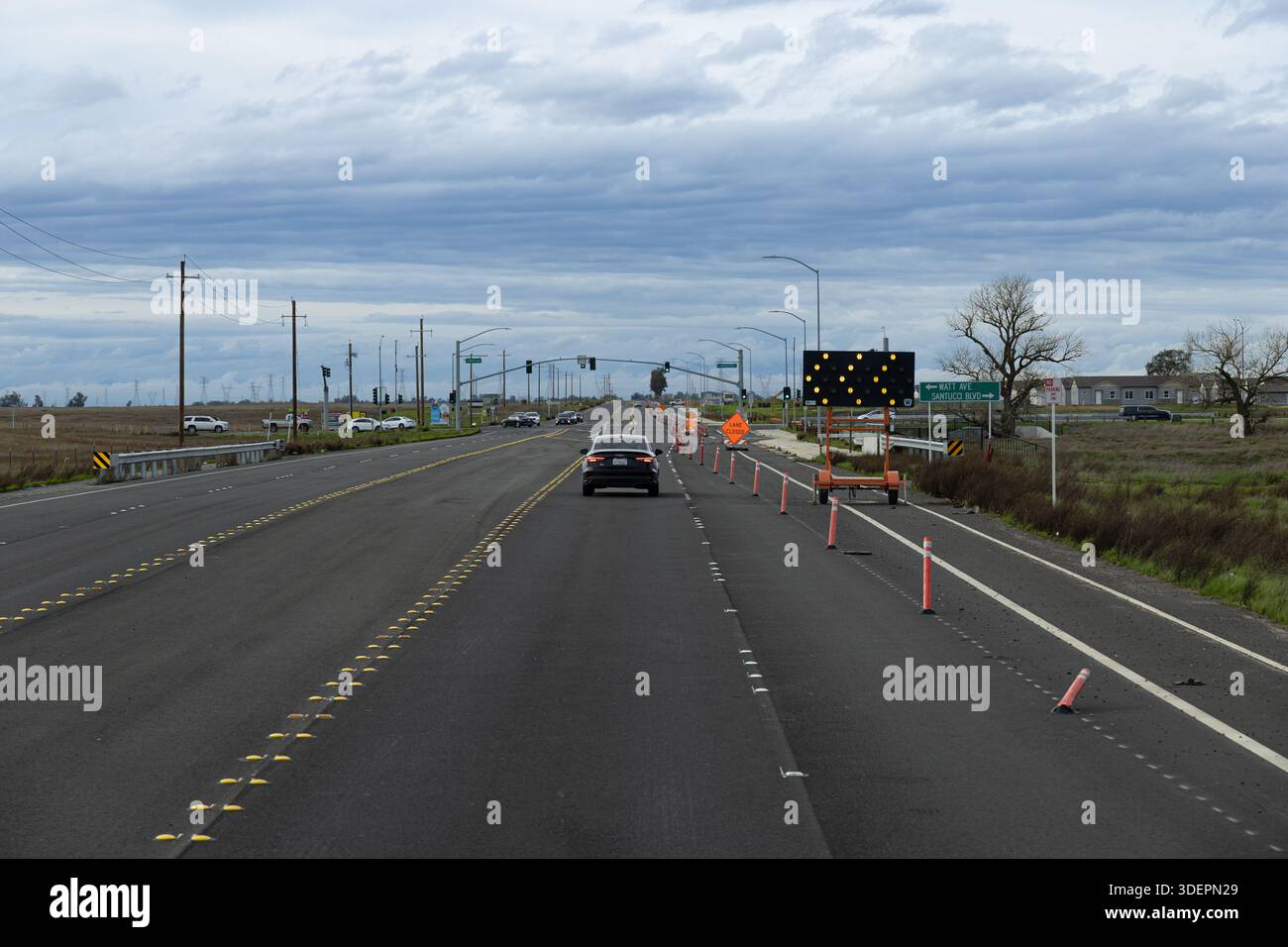 Les véhicules circulent le long d'une autoroute où la construction est en cours. Les cônes de circulation et les panneaux orientent les conducteurs au fur et à mesure que le travail est effectué. Banque D'Images