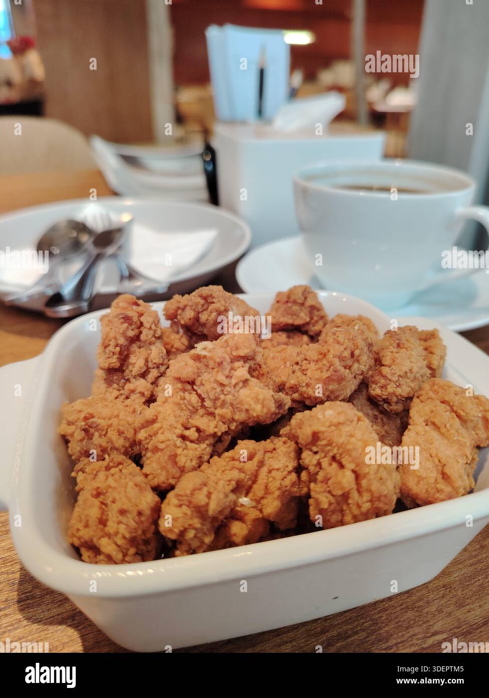 Poulet popcorn frit croquant dans un bol blanc, servi sur une table de café avec un fond de tasse de café flou. Banque D'Images