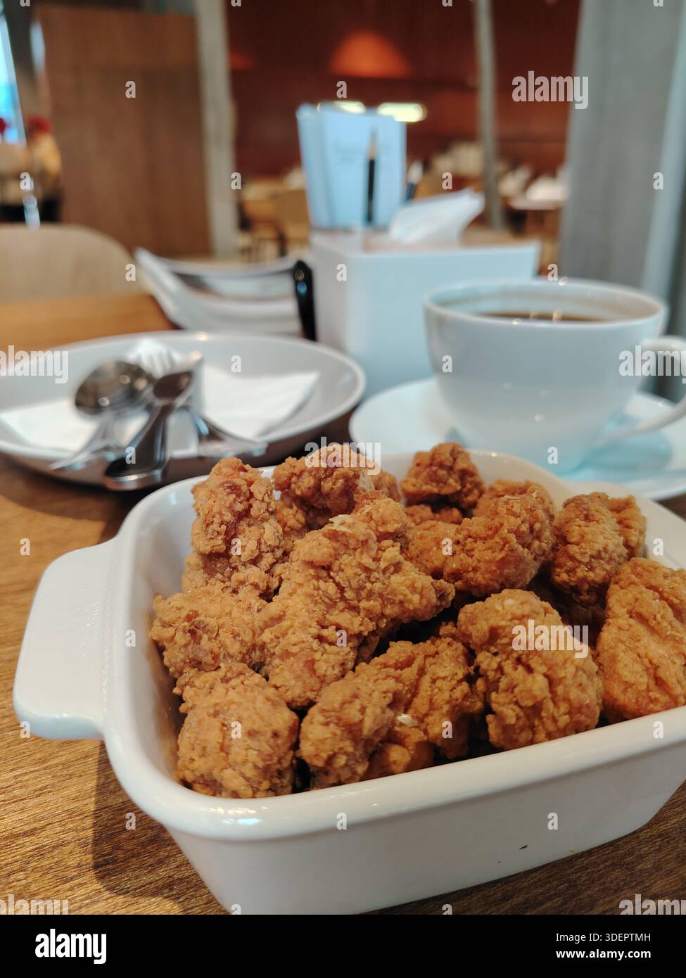Poulet popcorn frit croquant dans un bol blanc, servi sur une table de café avec un fond de tasse de café flou. Banque D'Images