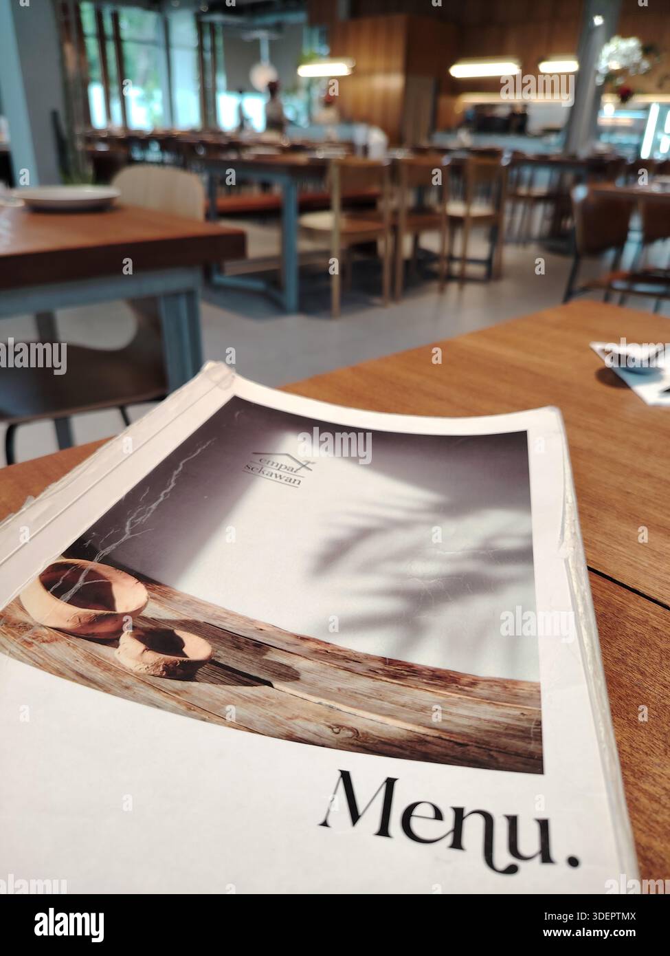 Un menu de restaurant élégant sur une table en bois, avec un intérieur de café flou avec un éclairage ambiant chaleureux. Banque D'Images