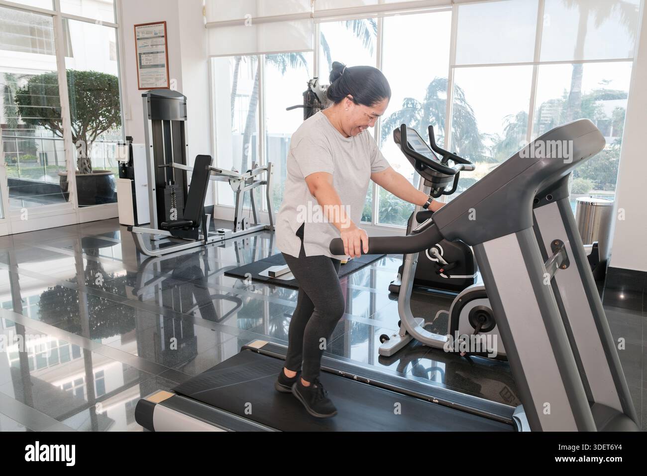 Une femme court sur un tapis roulant dans un centre de conditionnement physique entouré d'équipement de gymnastique. Elle a l'air concentrée et engagée dans sa routine d'entraînement le matin Lig Banque D'Images