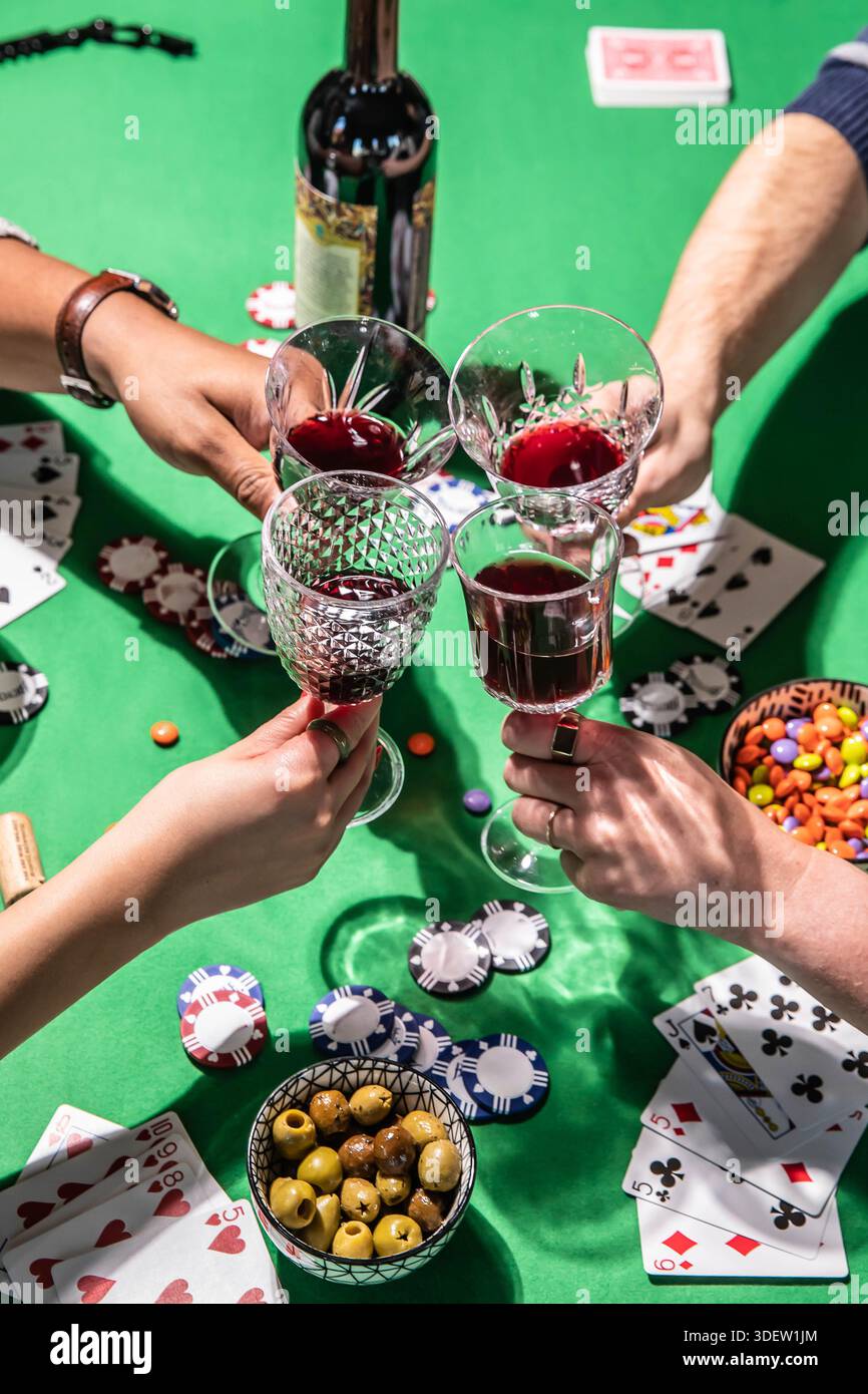 Amis grillant du vin tout en jouant au poker sur la table verte Banque D'Images