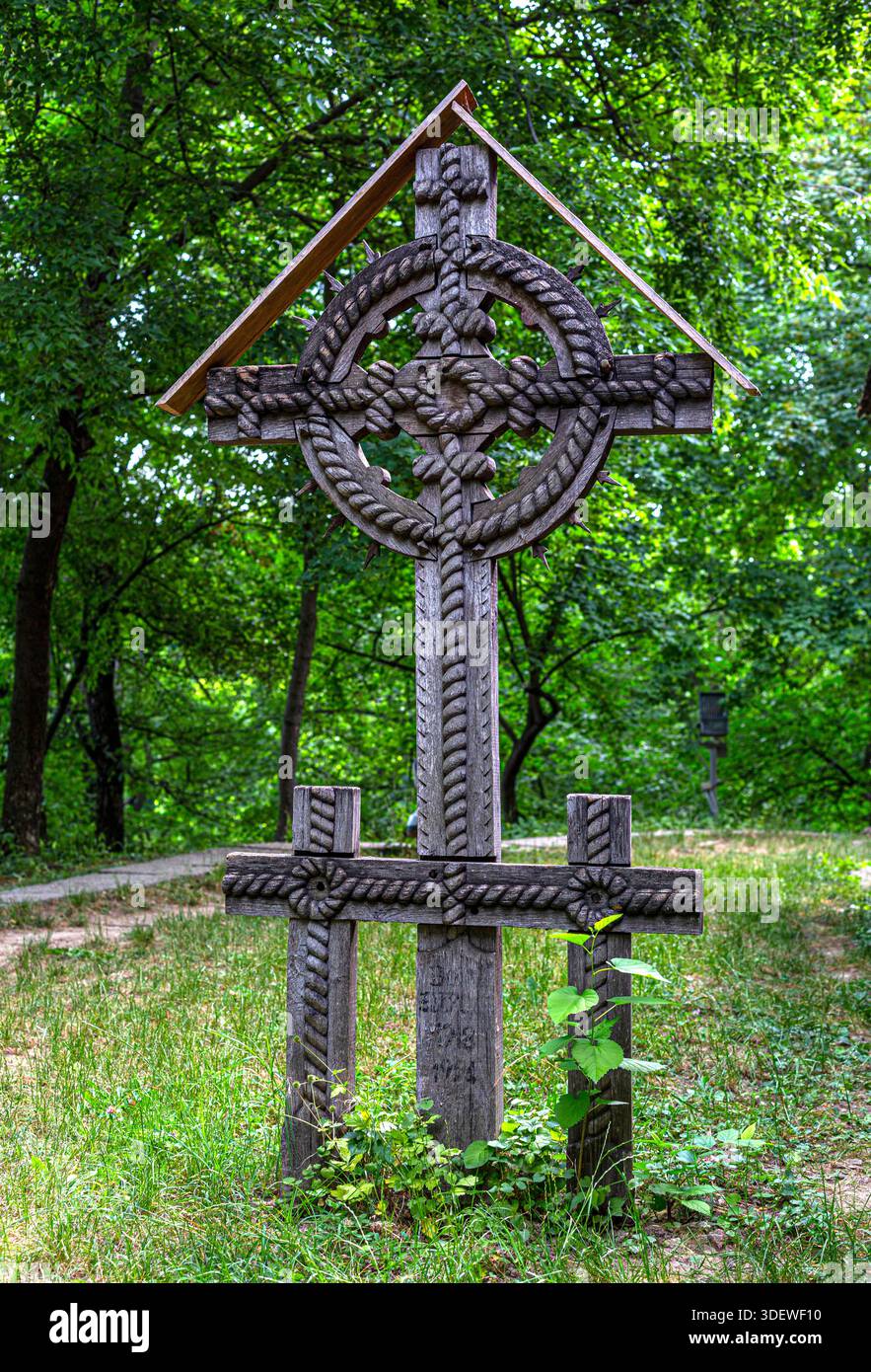 Croix celtique en bois sculptée à la main ornée debout dans un cimetière forestier vert Banque D'Images