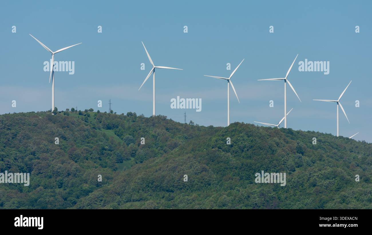Éoliennes sur une colline verte sous un ciel bleu clair. Banque D'Images