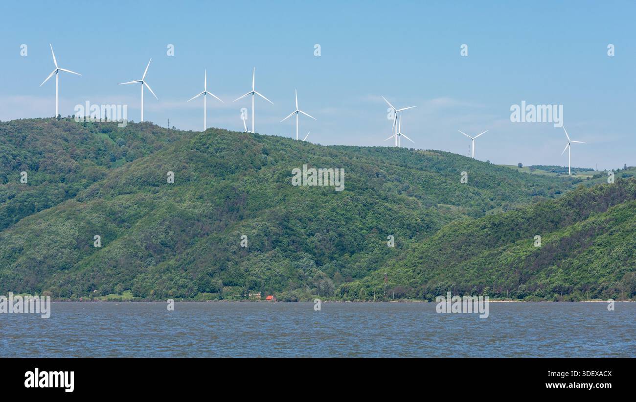 Éoliennes sur une colline verdoyante près d'un lac sous un ciel clair. Banque D'Images