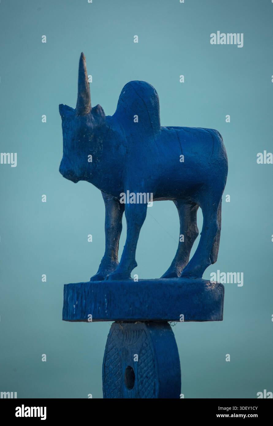 Sculpture sur bois - un poteau surmonté d'une sculpture d'un zébu et peint en bleu. La sculpture sur bois d'un poteau avec un zébu sur le dessus est une forme importante d'art traditionnel à Madagascar, en particulier dans le sud et l'ouest de l'île. Ces sculptures sont principalement associées aux rituels funéraires et ont une signification culturelle profonde. Les poteaux en bois sculptés sont connus localement sous le nom d'aloalo. Ce sont des éléments essentiels des tombes traditionnelles du sud et de l'ouest de Madagascar, en particulier parmi les peuples Mahafaly et Sakalava. Way Bay, Madagascar Banque D'Images
