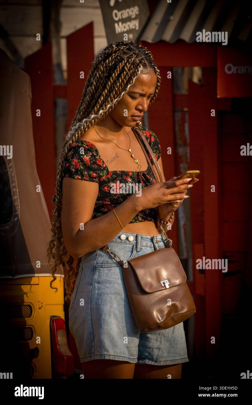 Une malgache utilisant son smartphone portable, Morondava, Madagascar. L'image montre comment les individus à Madagascar adoptent la technologie mobile pour rester connectés et s'engager dans un monde plus large, mettant en évidence l'évolution numérique continue du pays. Malgré l’amélioration des infrastructures, le coût élevé des données et des appareils reste un obstacle important pour de nombreux Malgaches. Banque D'Images