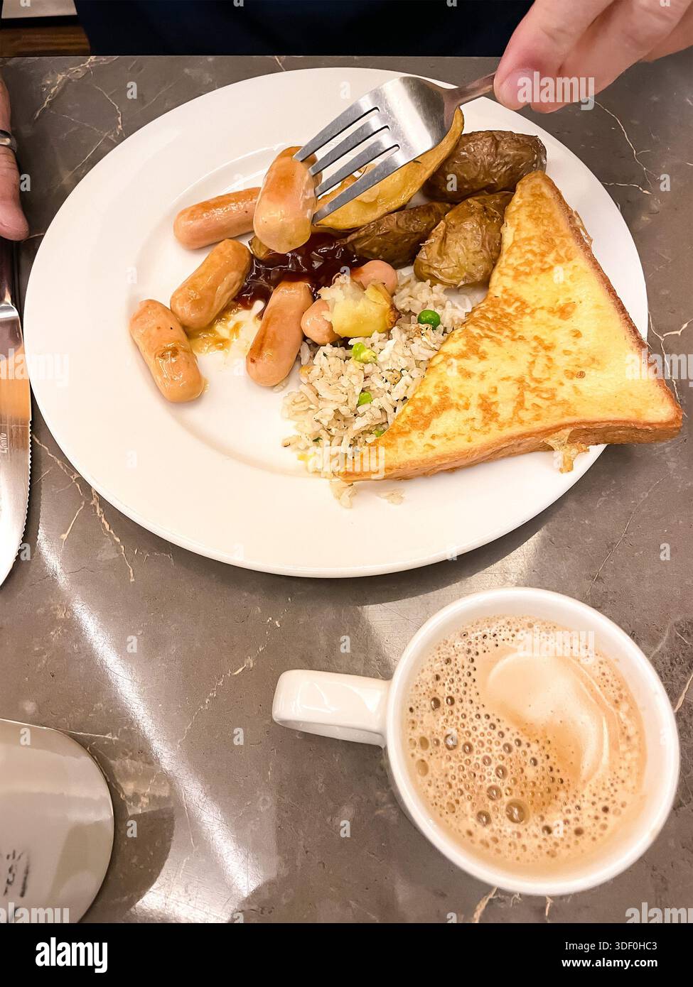 Assiette avec mini saucisses, pain grillé, pommes de terre rôties, riz et légumes servis avec une tasse de café sur une table en marbre malaisie Banque D'Images