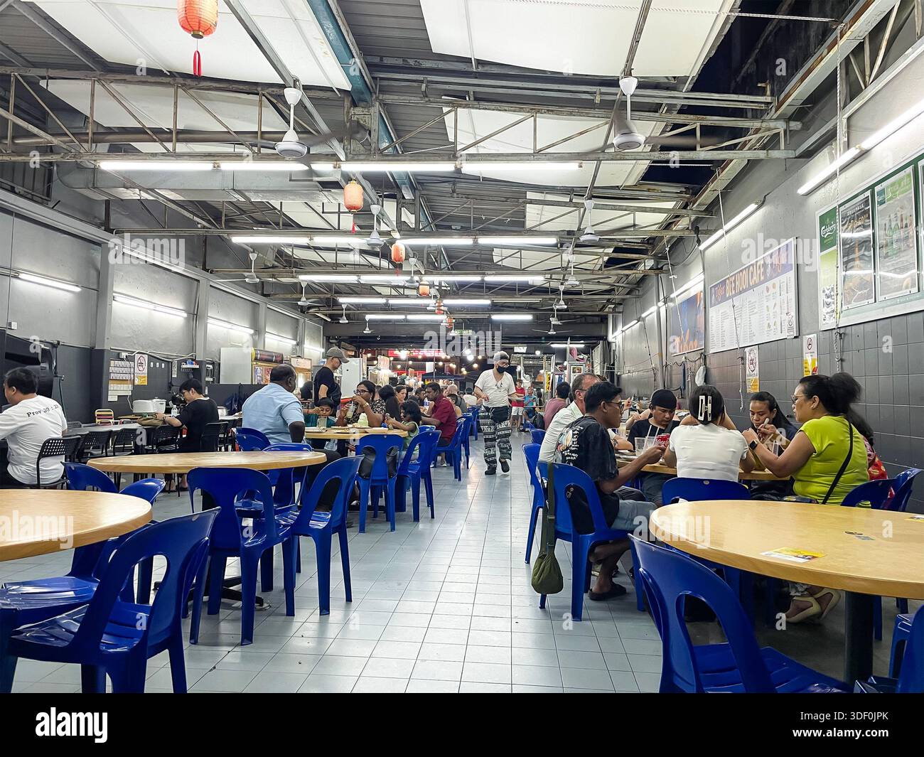 Aire de restauration de rue intérieure les gens dînent sur des tables et des chaises en plastique sous éclairage fluorescent et structure de plafond exposé georgetown penang malaisie Banque D'Images