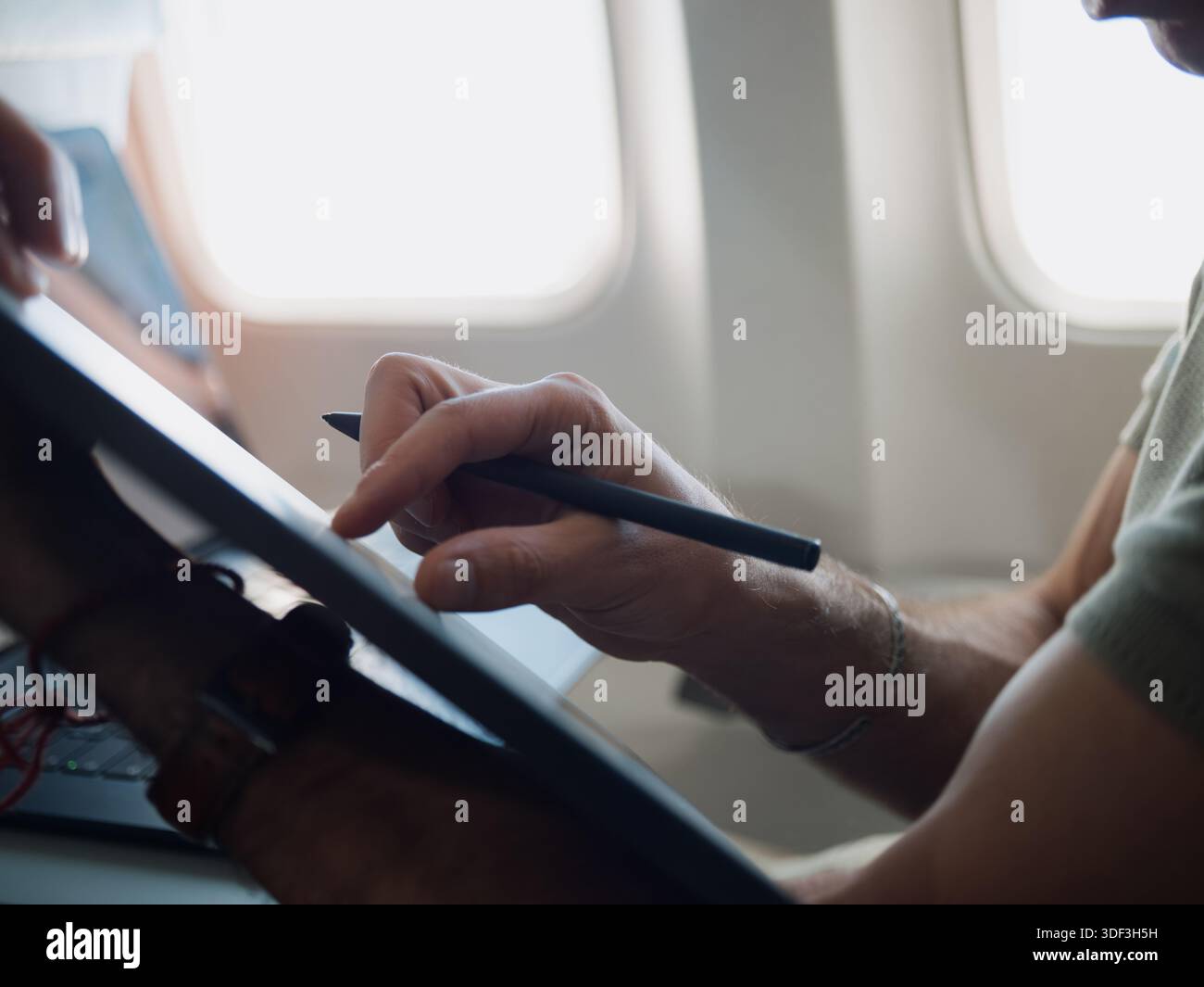 Personne utilisant une tablette et un stylet sur un siège d'avion, représentant la créativité mobile et le travail pendant le voyage. Banque D'Images