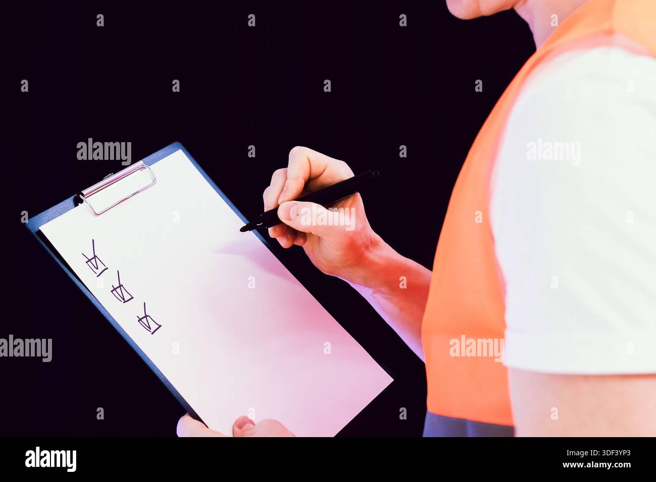 Travailleur de la construction vêtu d'un gilet orange à l'aide d'un stylo pour marquer les articles sur la liste de contrôle du presse-papiers. Banque D'Images