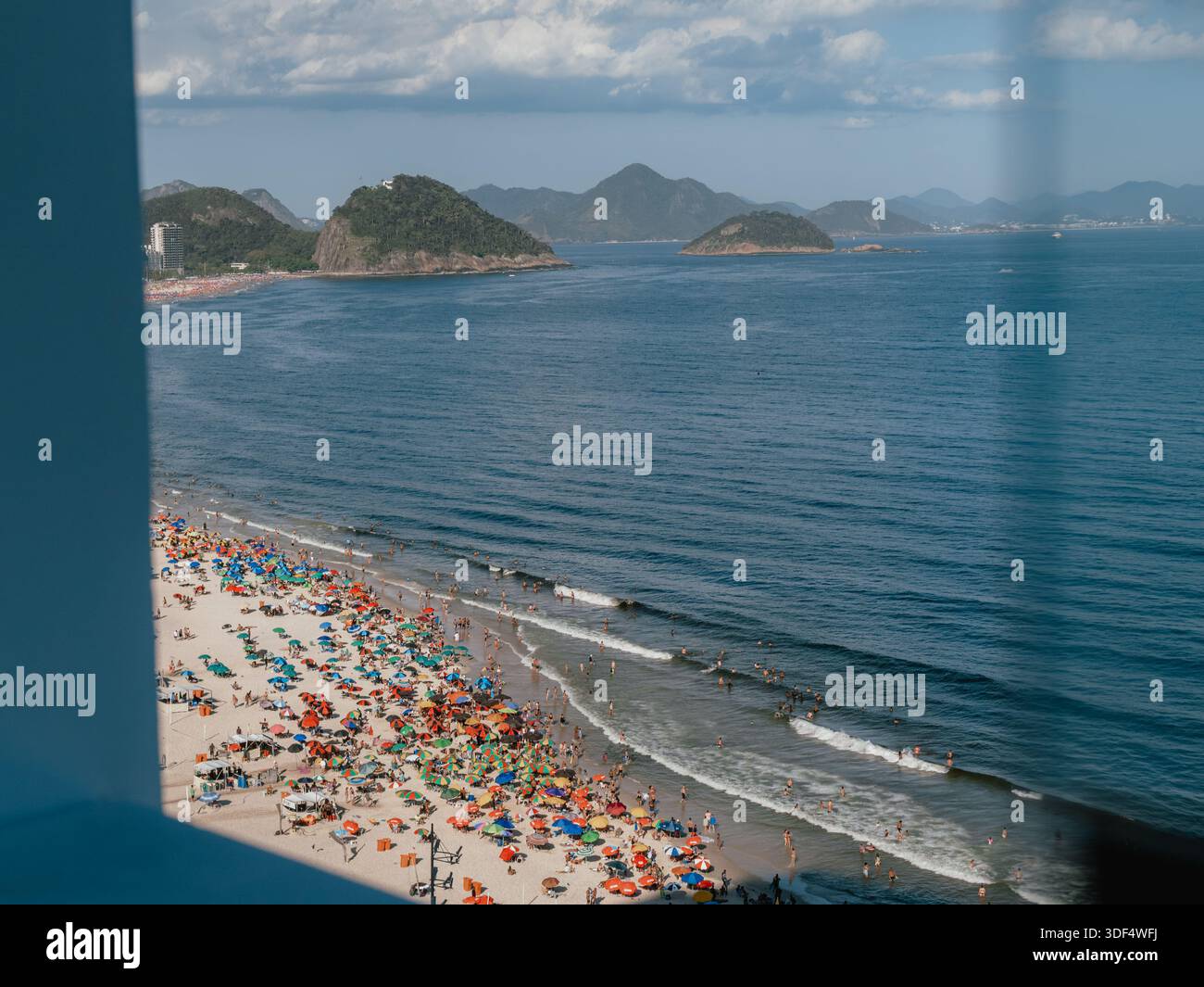 Plage bondée avec des parasols encadrés par une structure bleue, avec l'océan et le littoral au-delà. Banque D'Images