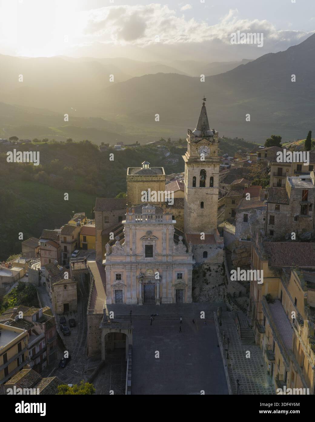 Vue aérienne de la Chiesa Madre di San Giorgio Martire debout majestueusement sur fond de montagnes vallonnées baignées dans la lumière dorée, CAC Banque D'Images