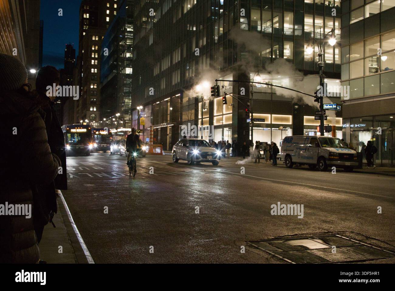 Un cycliste mène un flot de circulation sur Madison Avenue la nuit, leur phare perçant l'obscurité dans un moment nettement capturé du mouvement de New York. Banque D'Images