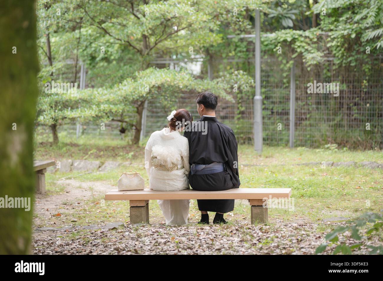 Couple portant un kimono et un yukata assis sur un banc dans un parc verdoyant. Kyoto, Japon. Banque D'Images