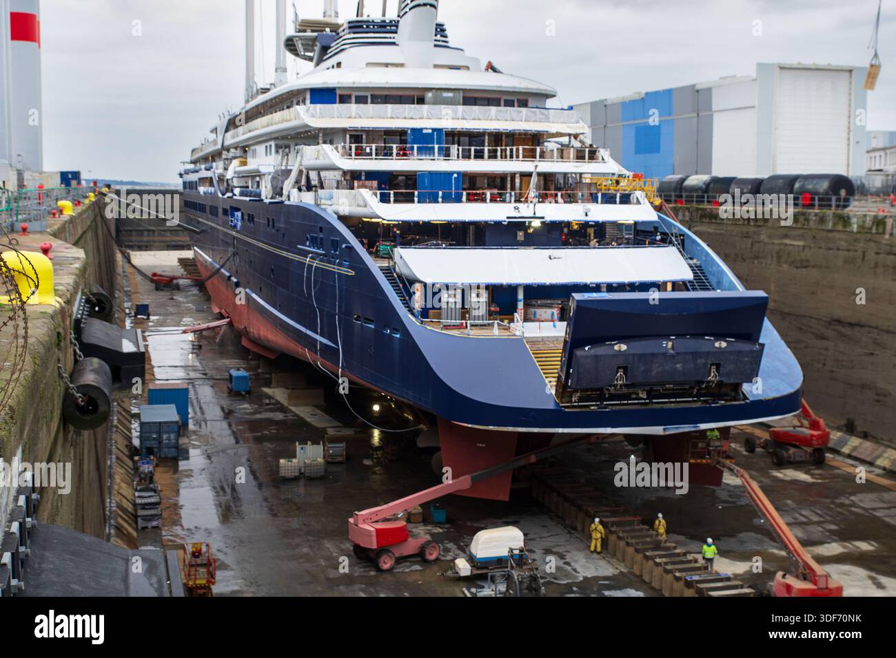 Un cargo écologique avec des mâts pour les voiles en cale sèche dans un chantier naval de Saint Nazaire, France, avec des grues et du matériel de construction ou de réparation Banque D'Images