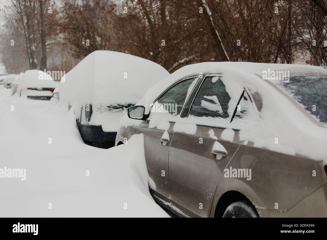 Une rangée de voitures garées complètement recouvertes d'une épaisse couche de neige après une forte chute de neige. Banque D'Images