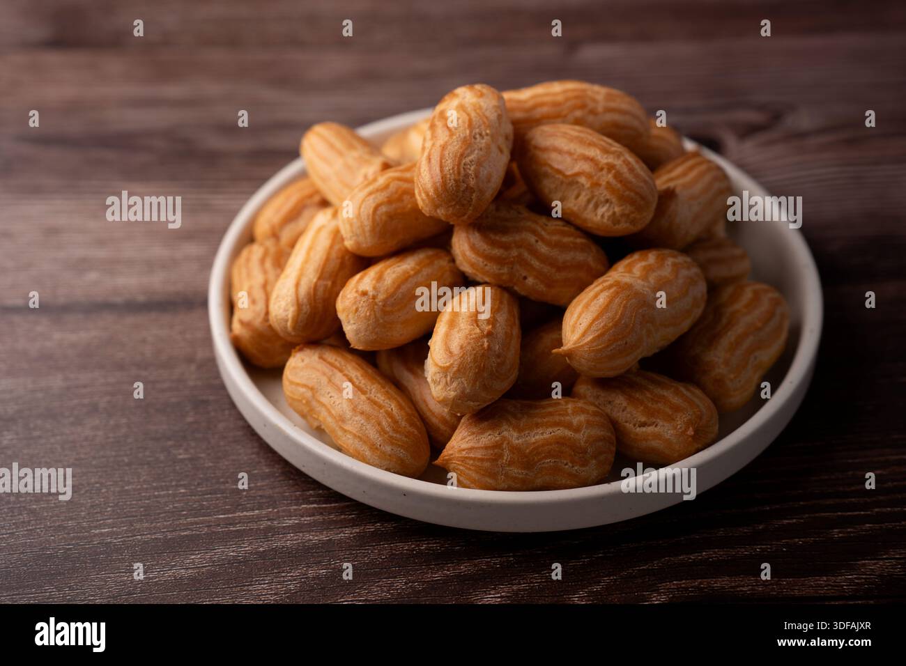 pile de mini pâtisseries dorées à choux disposées sur une simple plaque en céramique blanche reposant sur une table en bois sombre, lumière douce et chaude soulignant le tuyau strié Banque D'Images