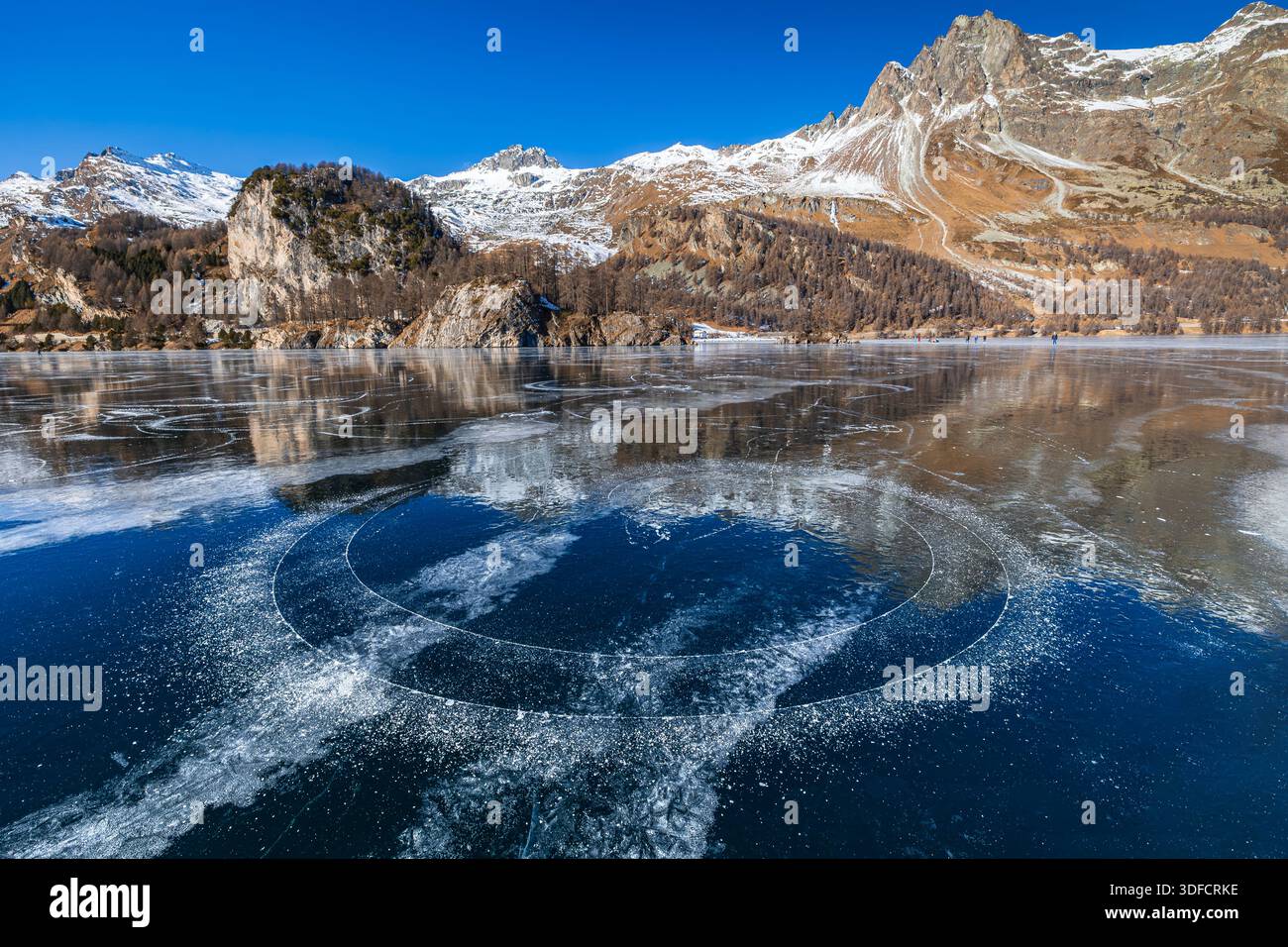 Piste de patinage en cercle traversant la ligne de glace blanche sur la surface de glace noire sur le lac gelé Silsersee à Moritz, haute Engadine, Suisse Banque D'Images
