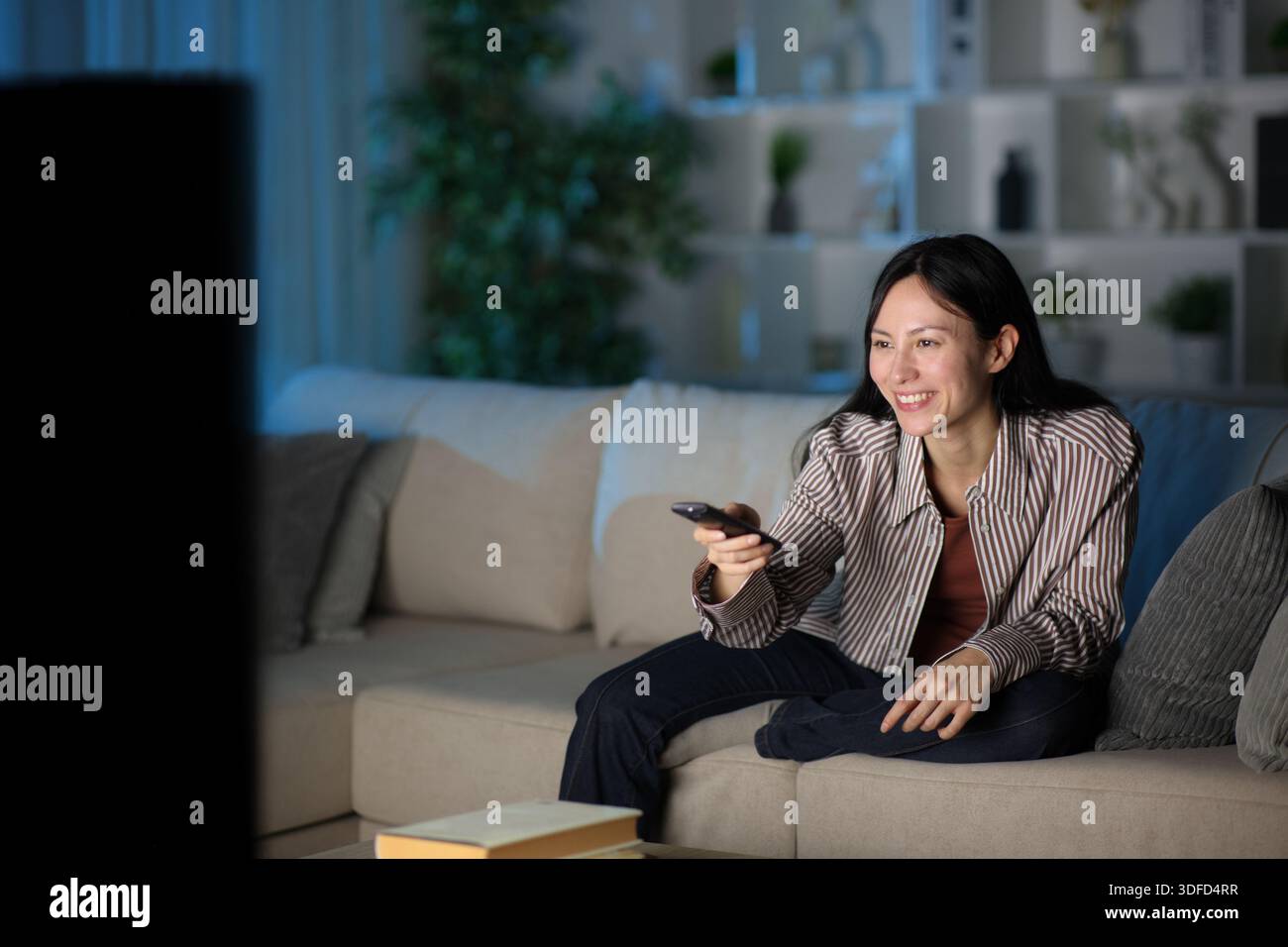 Femme asiatique heureuse utilisant la télécommande regardant la télévision dans la nuit à la maison Banque D'Images