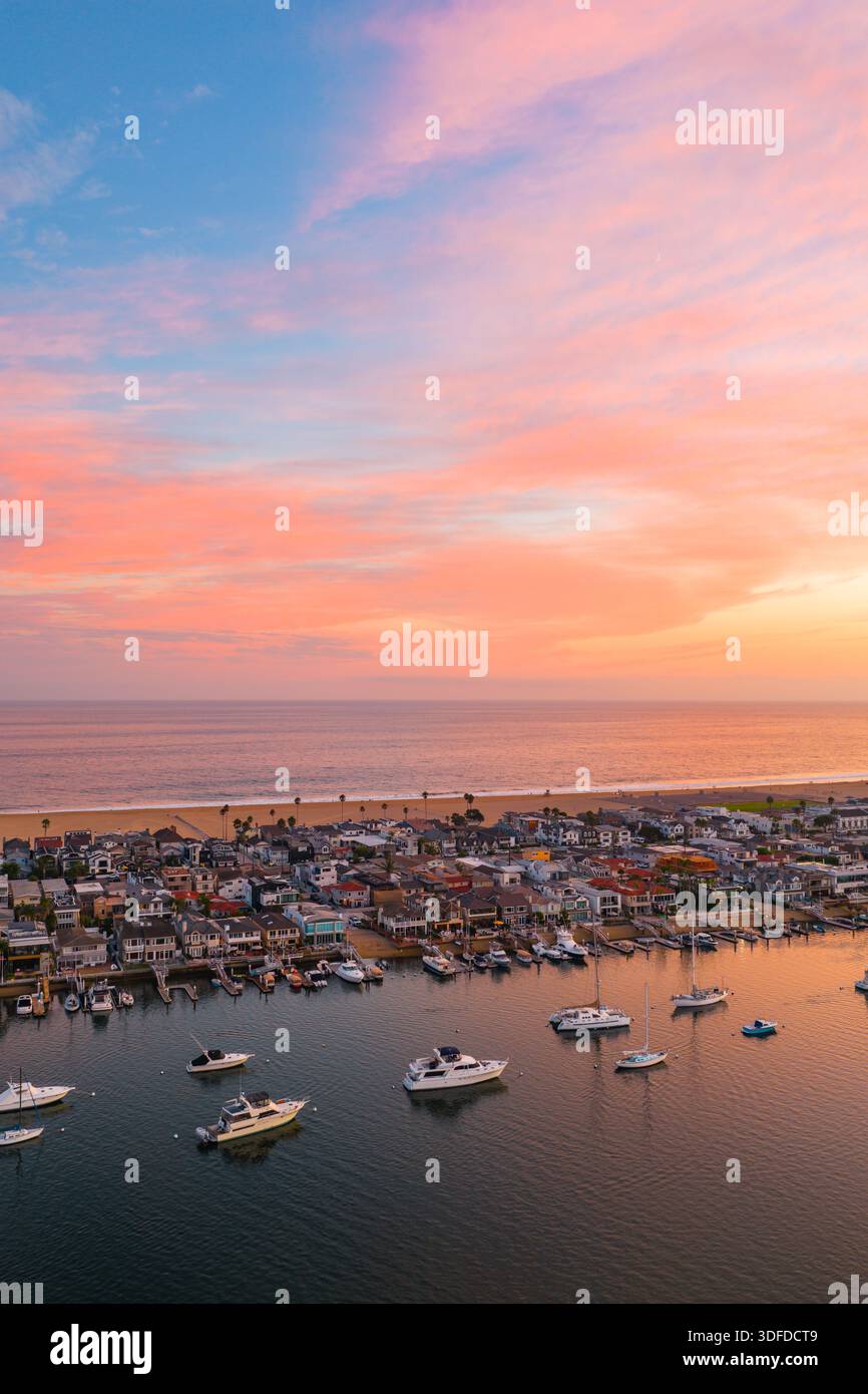 Vue aérienne des bateaux amarrés dans le port alors que le ciel flambe avec des teintes de coucher de soleil flamboyantes sur la côte lointaine, Newport Beach, Californie, États-Unis Banque D'Images