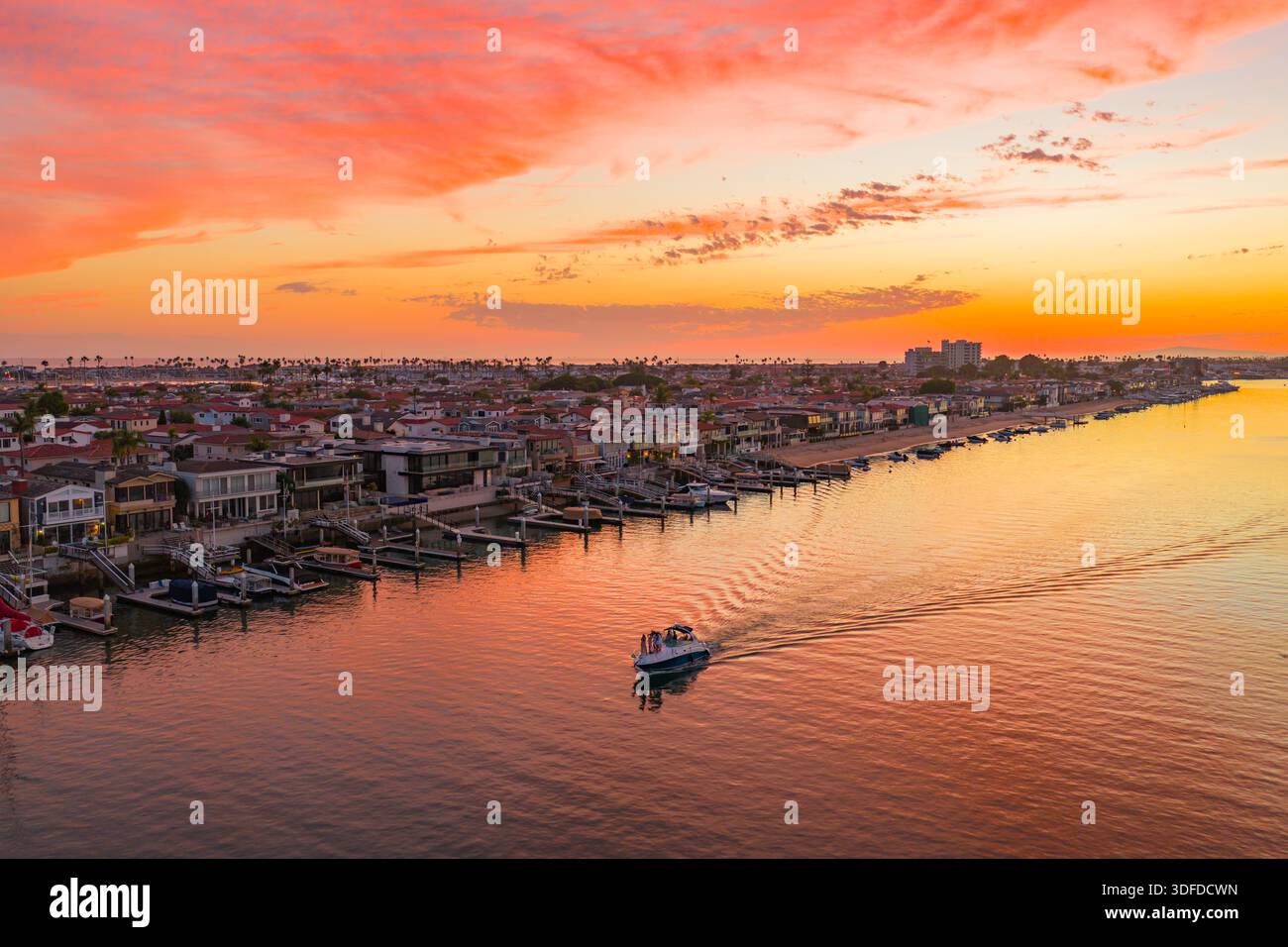 Vue aérienne des bateaux glissent le long des eaux tranquilles, encadrées par les teintes vibrantes du coucher de soleil jetant une lueur dorée sur la côte, Newport Beach, CA Banque D'Images