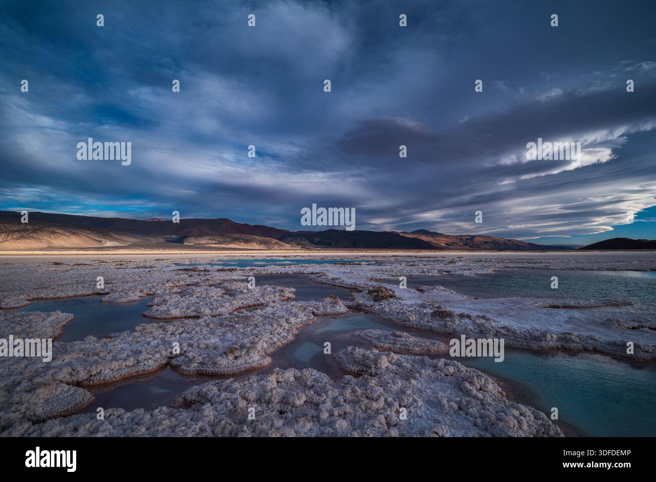 Plan grand angle haute résolution de formations salines et de piscines minérales sous un ciel crépusculaire spectaculaire et nuageux dans un paysage désertique. Banque D'Images