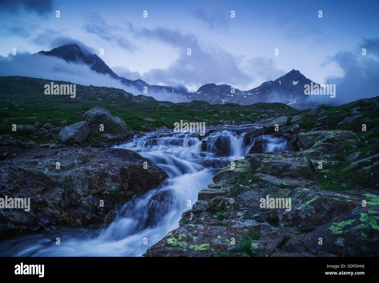 Photographie de paysage d'un ruisseau rocheux au premier plan avec des sommets montagneux couverts de brouillard en arrière-plan pendant le crépuscule. Banque D'Images