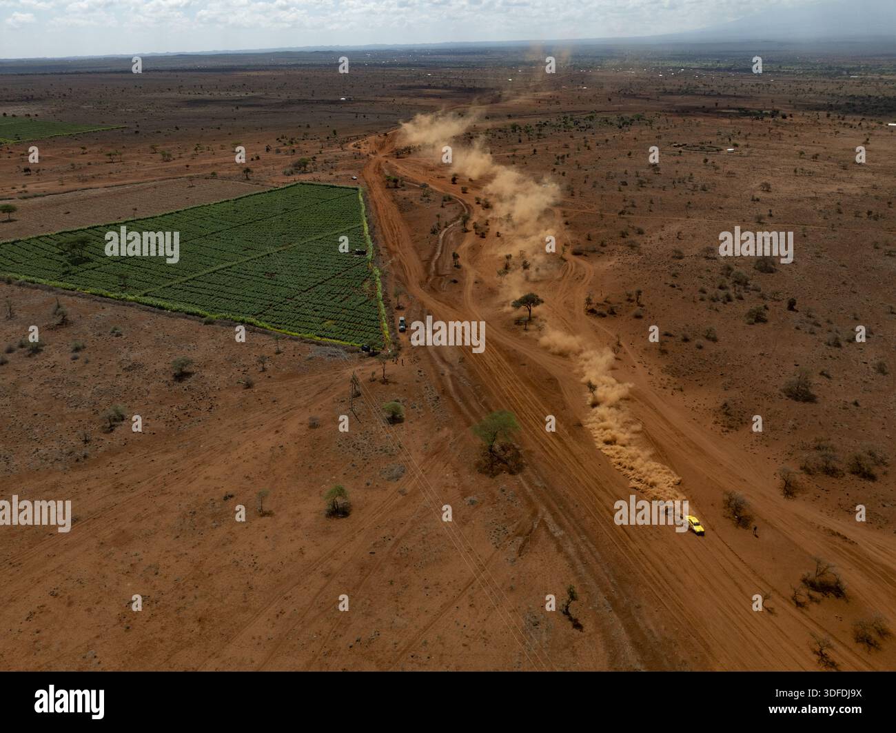 Diani, Kenya - 10 décembre 2025 : vue aérienne d'une route poussiéreuse traversant le paysage aride, contrastant avec un champ vert vibrant, sous un vaste Banque D'Images