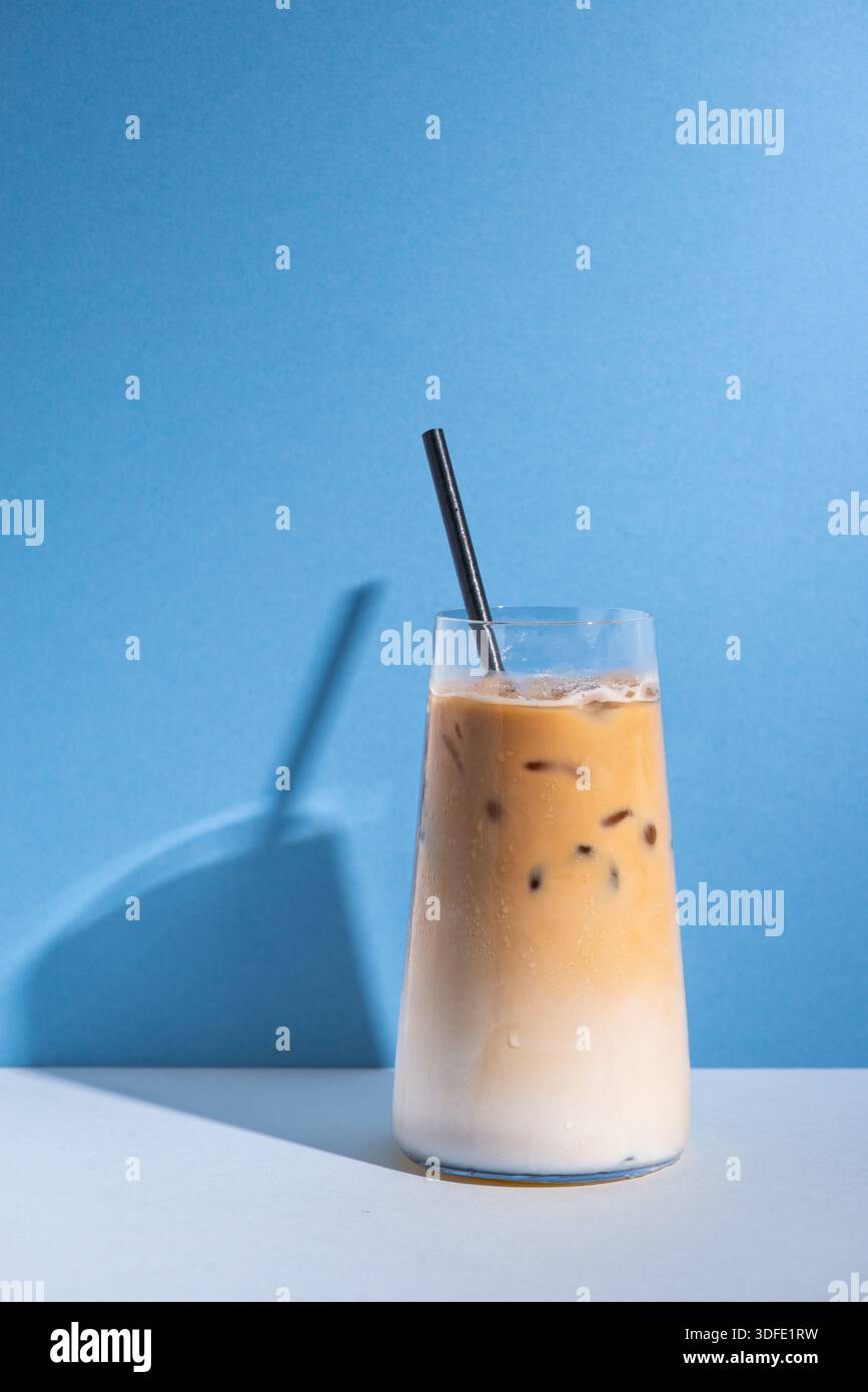 Latte glacé servi sur de la glace dans une tasse en verre transparent. Boisson au café crémeuse photographiée sur un fond de studio propre et minimal, idéal pour les menus de café. Banque D'Images