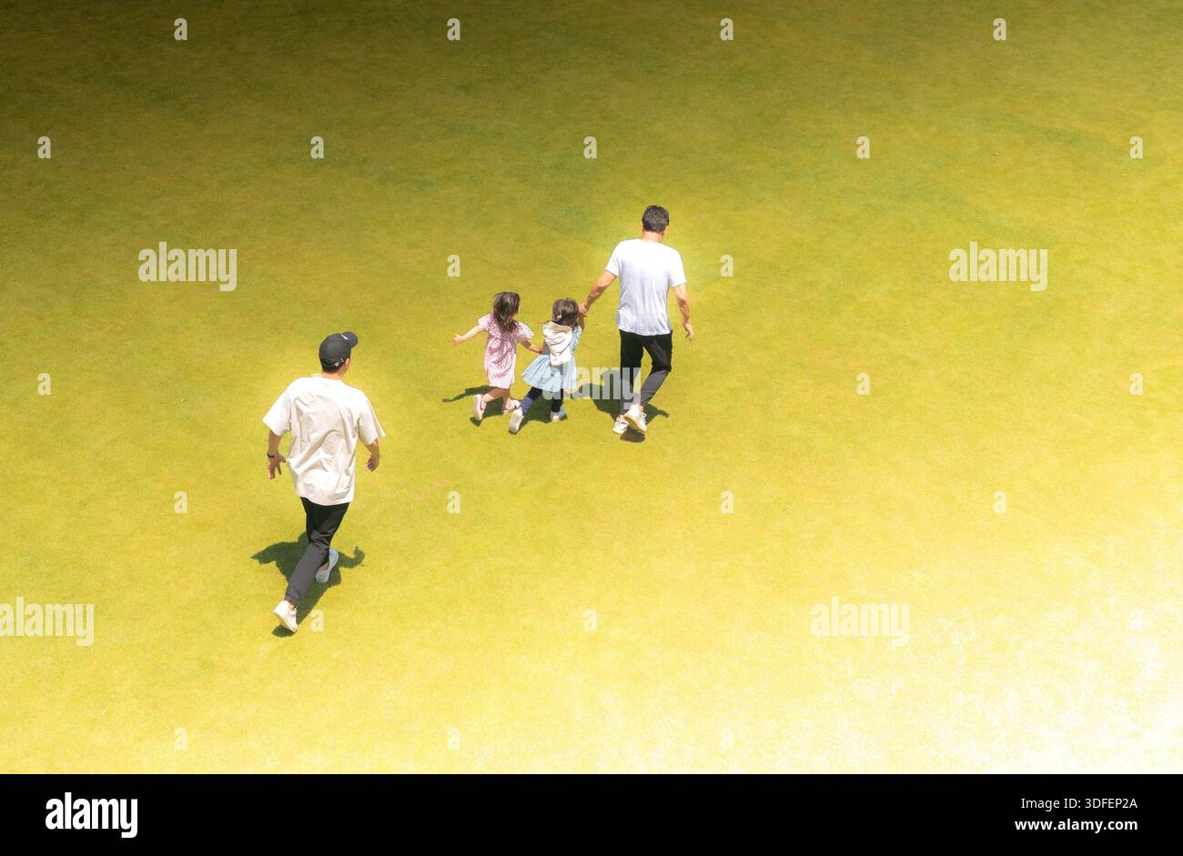 Vue d'une famille se promenant sur un champ vert vibrant sous le soleil chaud, leurs personnages projetant de longues ombres à Tokyo, Tokyo, Japon. Banque D'Images