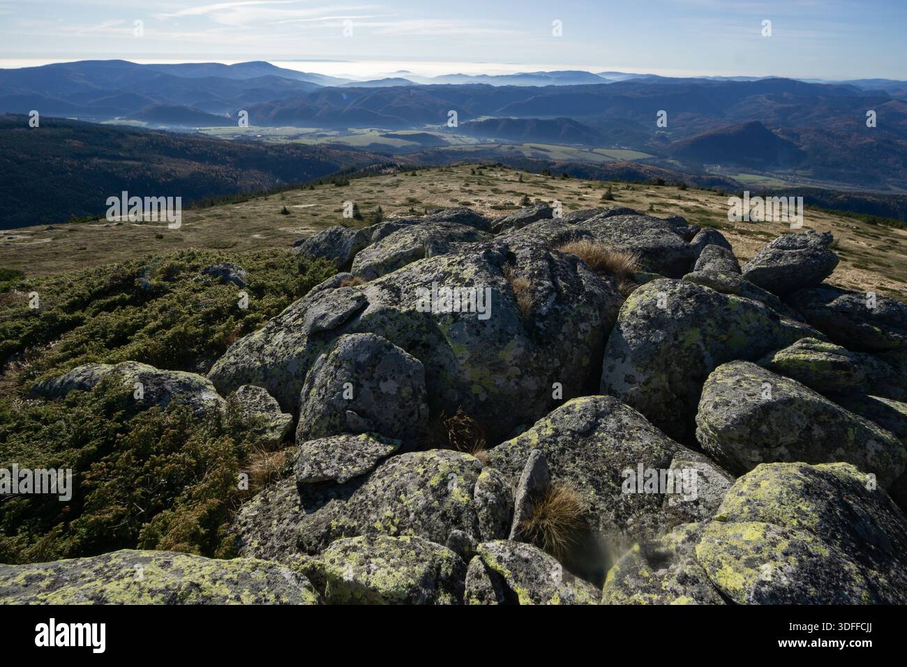 Vue de rochers couverts de lichens en cascade sur une colline, contrastant avec les montagnes brumeuses lointaines sous un ciel bleu pâle, Nizke Tatry, Banskobystri Banque D'Images
