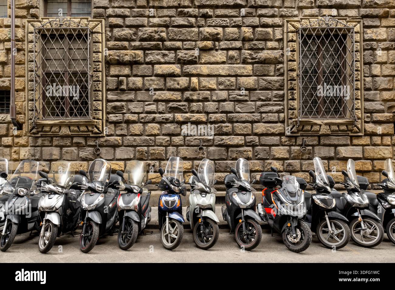 Une rangée de scooters et cyclomoteurs garés avec un bâtiment ancien ou médiéval comme arrière-plan à Florence, Italie. Banque D'Images