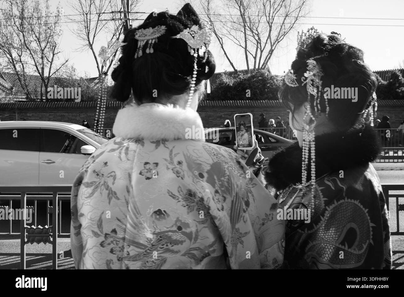 Deux femmes en costumes impériaux de l'ère Qing font une pause pour un selfie, des couronnes de phoenix ornées rencontrant des écrans de smartphone, où la tradition danse avec le numérique. Banque D'Images