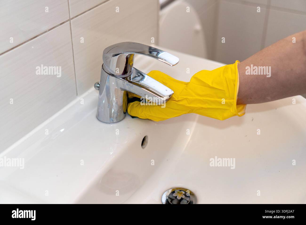 Processus de nettoyage de salle de bain : main dans le gant jaune polissant robinet chromé. Banque D'Images