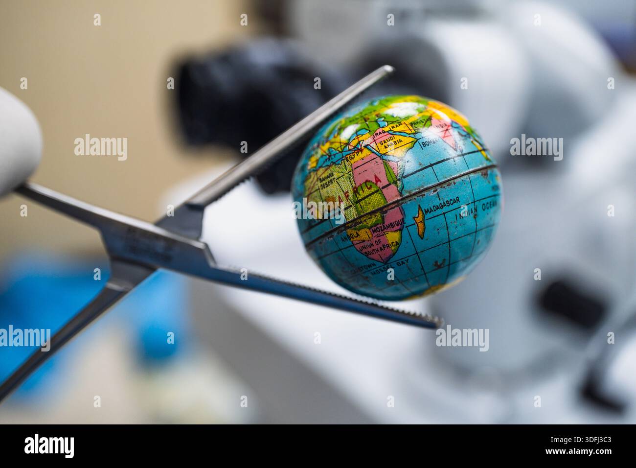 Un petit globe tenu par des ciseaux, symbolisant la précision et l'attention globale dans la science ou l'éducation Banque D'Images