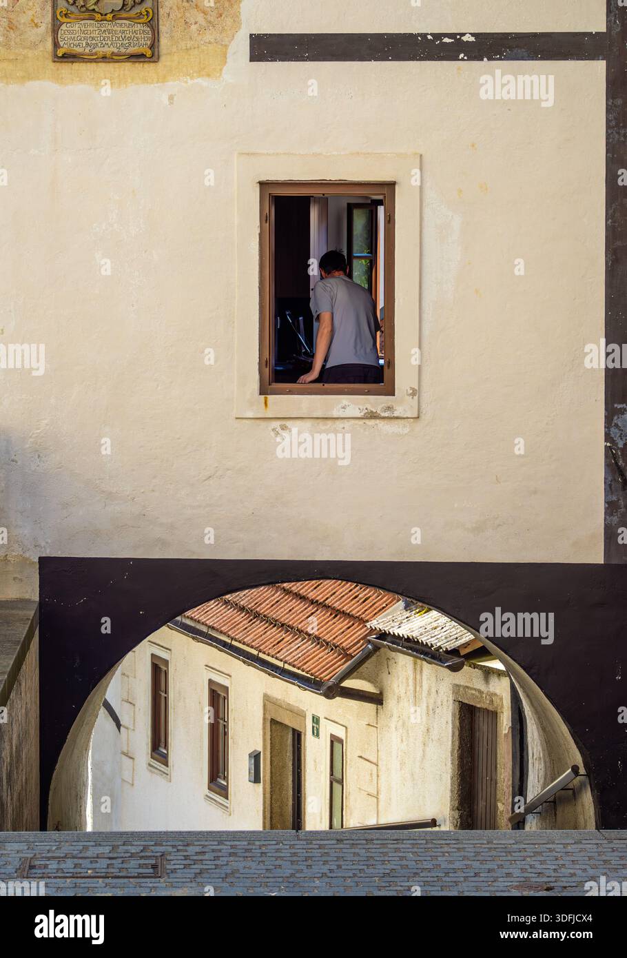 Skofja Loka, Slovénie - 30 juillet 2025 : personne vue à travers une fenêtre au-dessus d'une ruelle voûtée. Banque D'Images