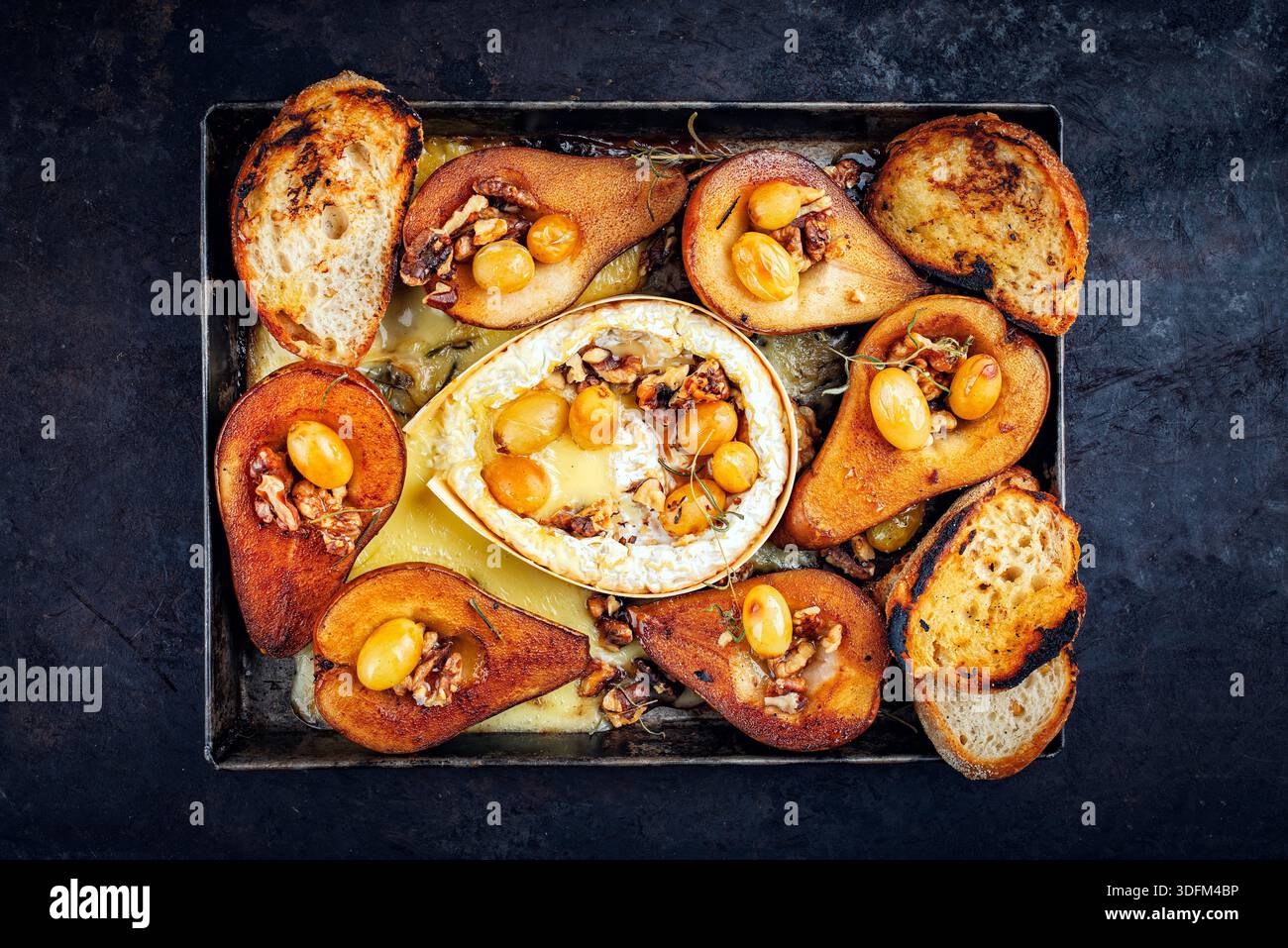 camembert cuit au four avec poires glacées caramélisées, noix et raisins et baguette servie sur une assiette en métal rustique Banque D'Images