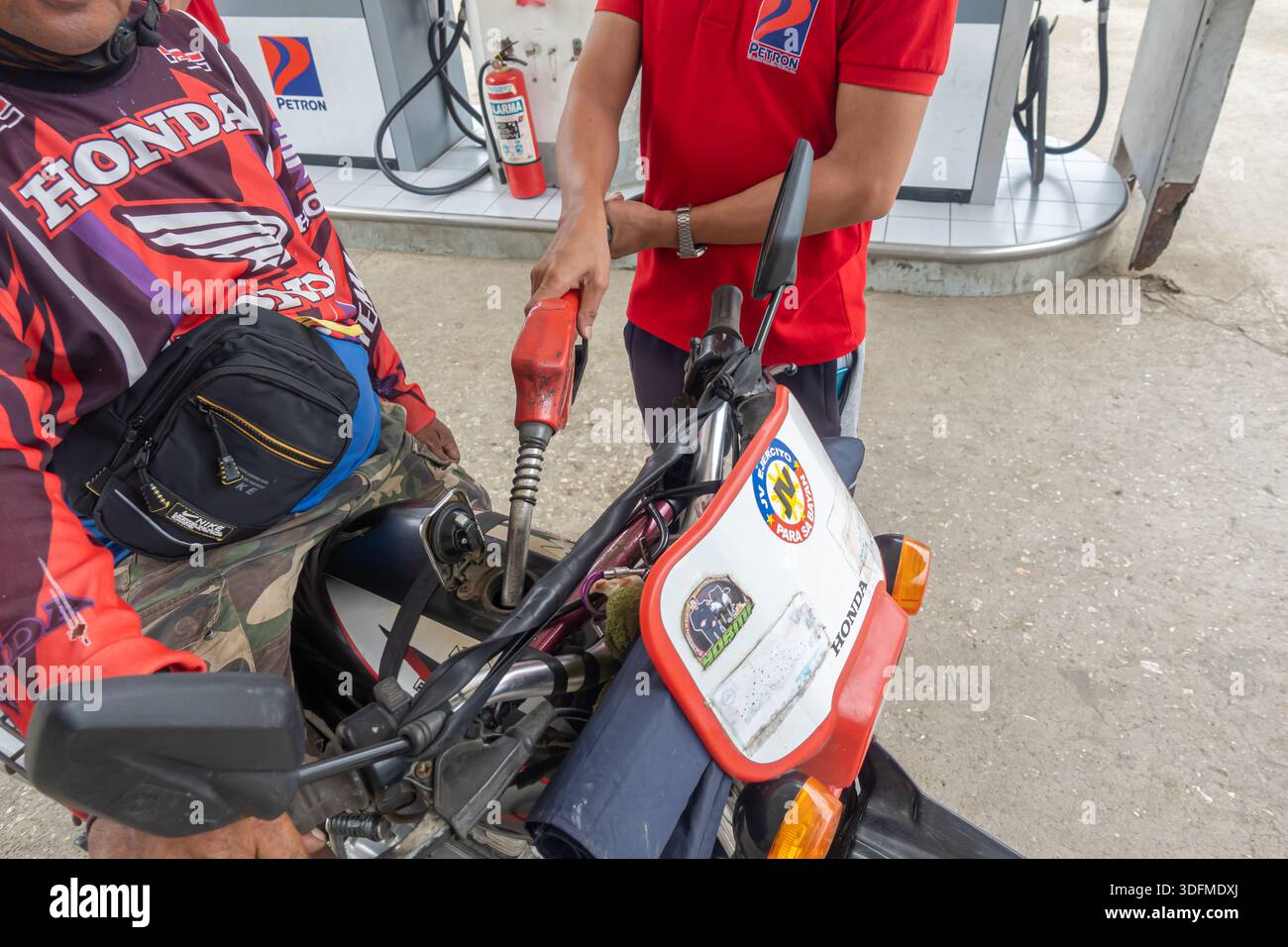 Employé de Petron ravitaillant une moto dans une station-service, Bohol, Philippines. Le procédé consiste à insérer une buse de carburant dans le réservoir de la moto. Banque D'Images