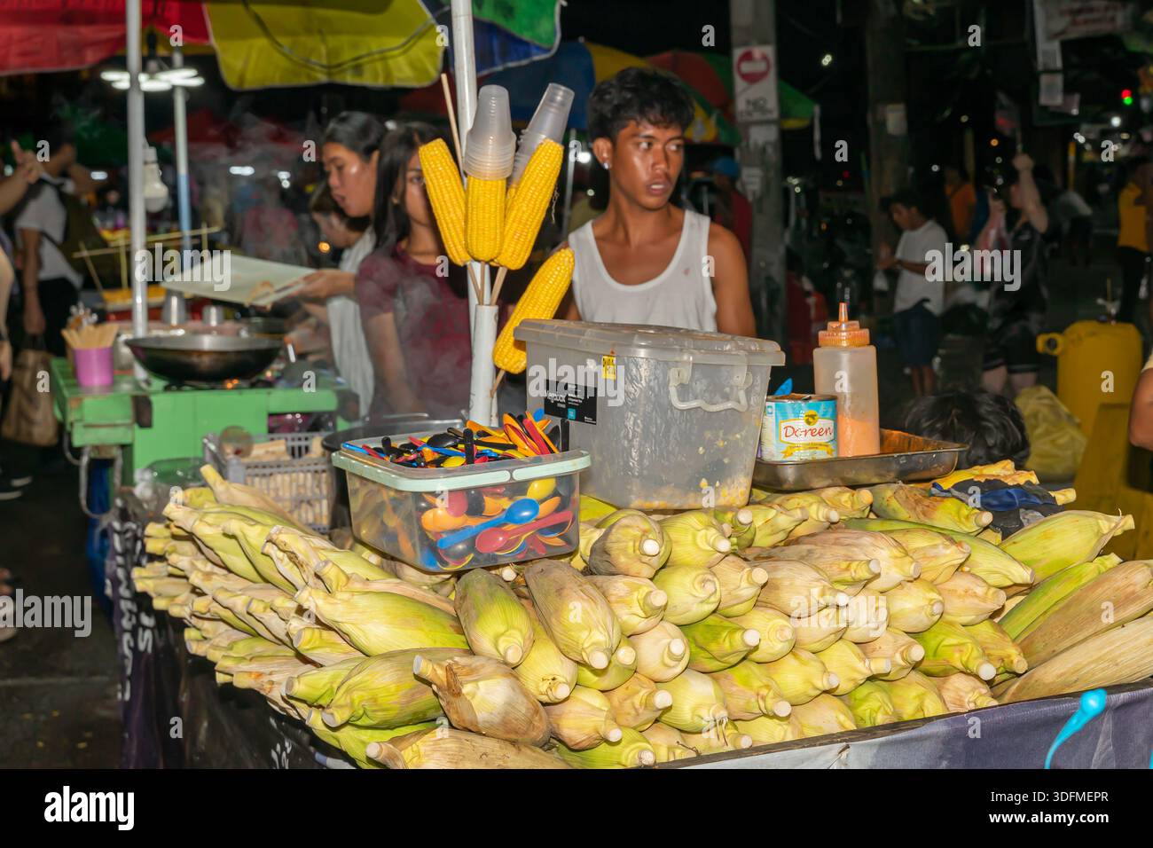 Vendeur de rue vendant du maïs sur l'épi d'un chariot de rue la nuit dans la ville de Cebu. Environnement typique du marché alimentaire de rue aux Philippines. Banque D'Images