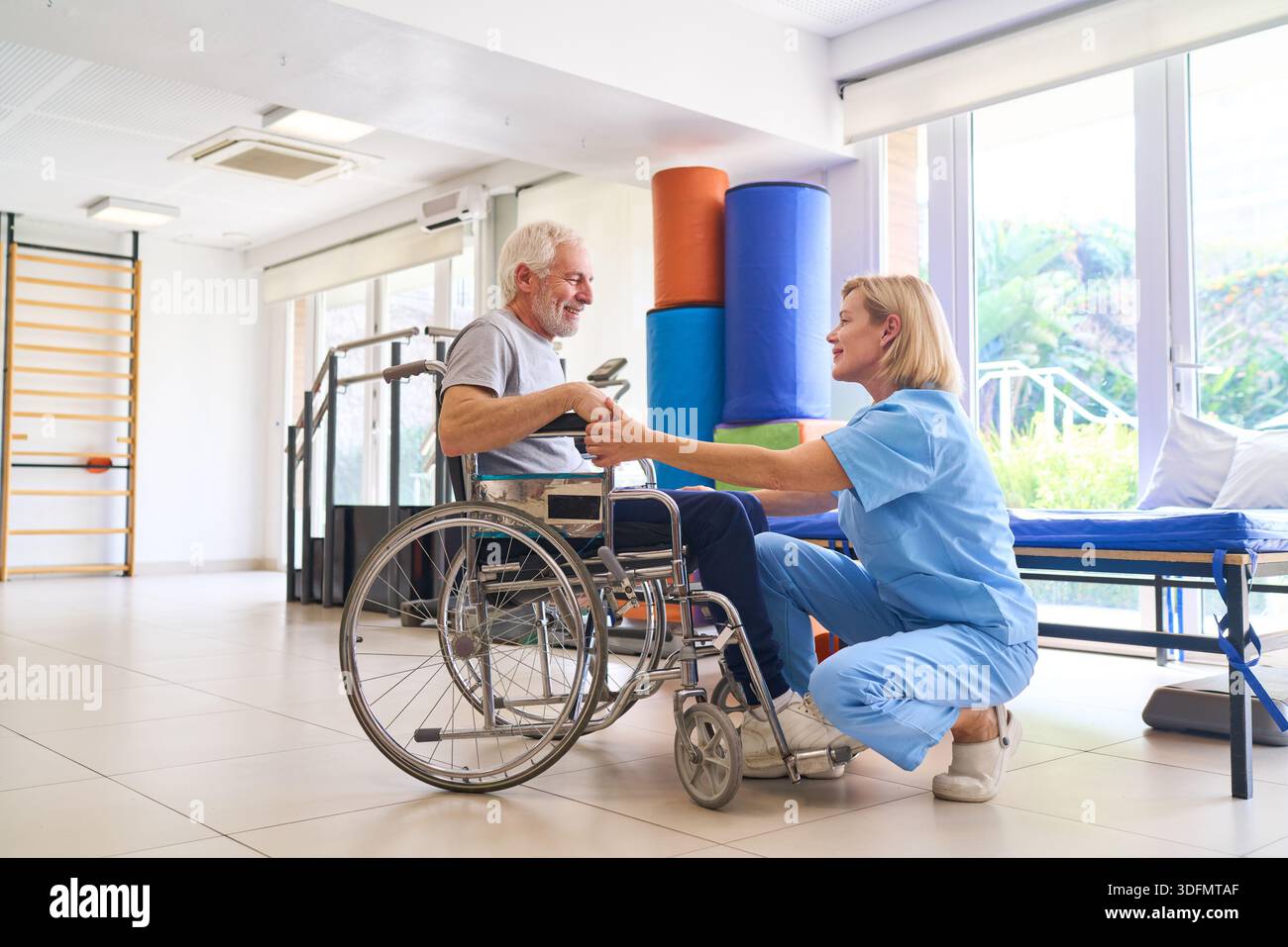 Un homme âgé en fauteuil roulant reçoit l'aide d'un physiothérapeute dans un centre de réadaptation ils travaillent sur la récupération et la formation de mobilité indoo Banque D'Images