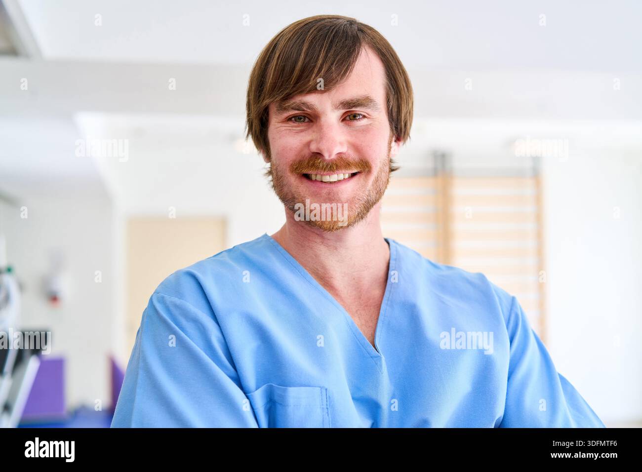 Portrait d'un physiothérapeute masculin souriant portant des gommages bleus dans un centre de réadaptation le professionnel de la santé est dans un cadre clinique prêt à Banque D'Images