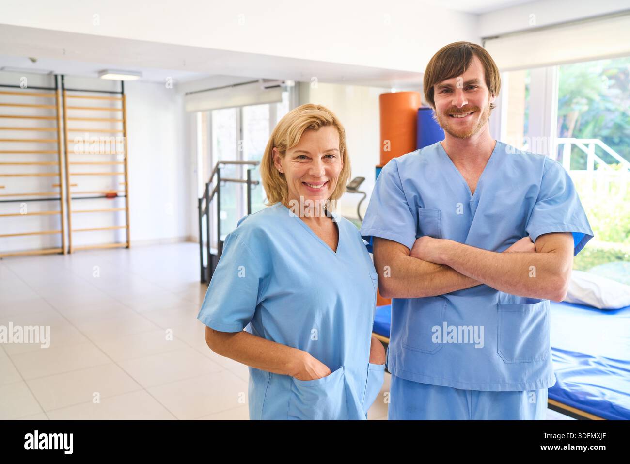 Portrait de deux physiothérapeutes souriants en uniformes bleus debout dans un centre de réadaptation les professionnels de la santé sont prêts à fournir des soins de santé et reh Banque D'Images