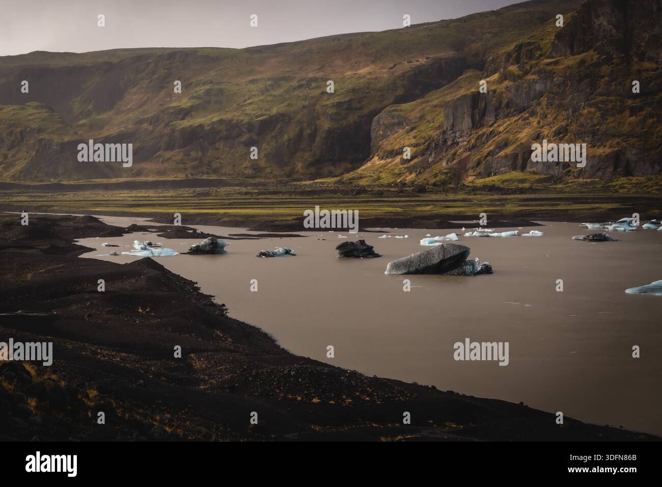 Vue de glace glaciaire dérivant sereinement sur le lac, juxtaposée aux sables noirs durs sous la montagne, île du Sud, Islande. Banque D'Images