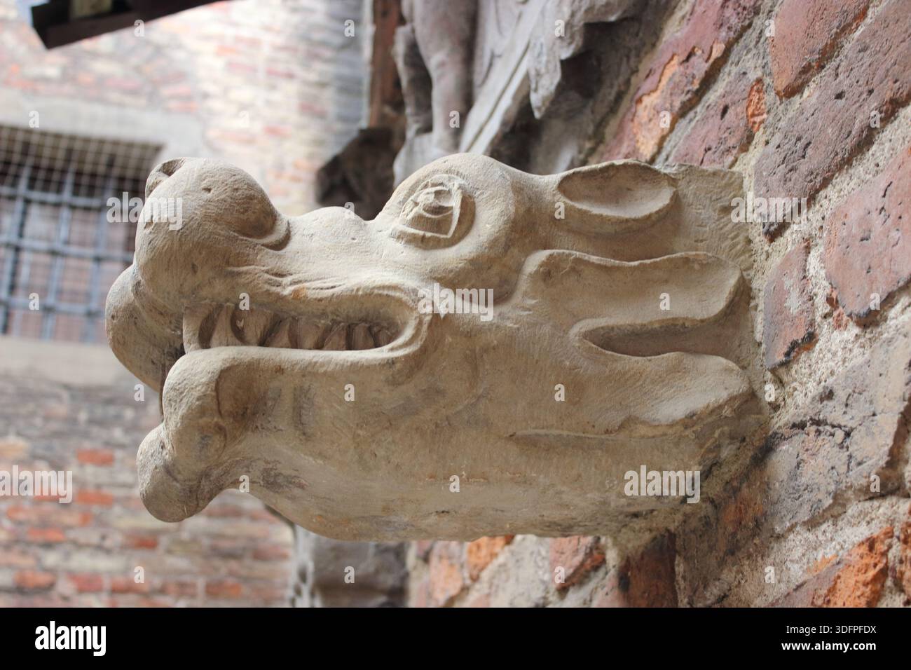 Gros plan d'une tête de gargouille en pierre projetant d'un mur de briques historique montrant des sculptures de style médiéval altérées et des détails architecturaux. Banque D'Images